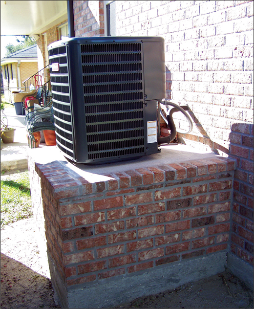 Air conditioning / heat pump compressor mounted on a brick pedestal outside an elevated home.