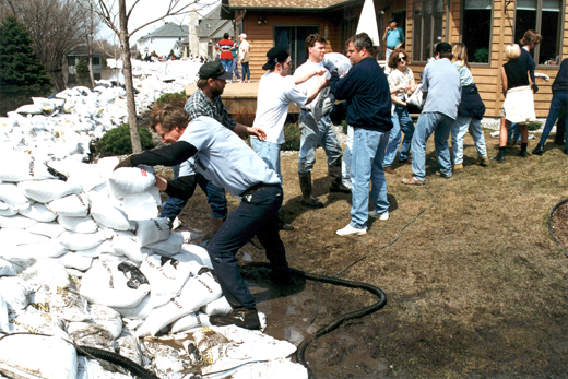 Sandbagging becomes a community effort as hundreds of residents and volunteers fight the rising waters of the Red River. Residents form a work line to build a sandbag barrier during a Red River flood in 1997.