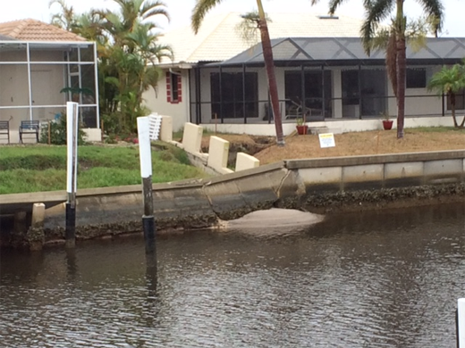 A concrete seawall with cracks that has partially collapsed in front of homes along a backyard canal in Florida.