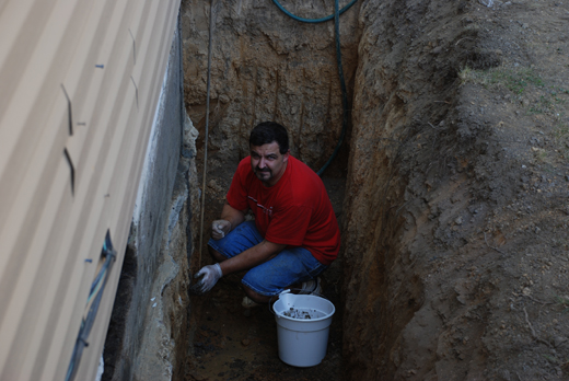 Deep trench dug to install a french drain. Man sitting in the trench preparing the area.