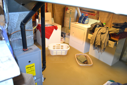 Basement flooded due to sewer back-up. Laundry baskets float in the dirty floodwater that still fills the space.