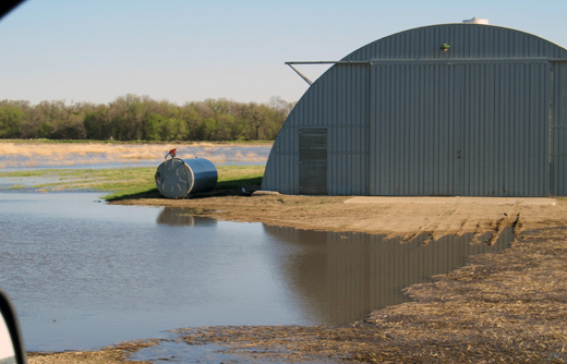 Agricultural building elevated on fill with water ponded in front.