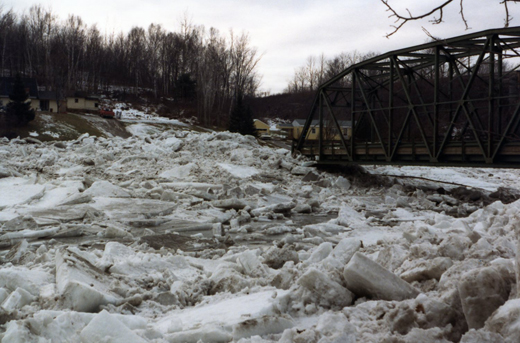 The ice nearly comes up to the base of the bridge and flows around the edge of the bridge onto the roadway.