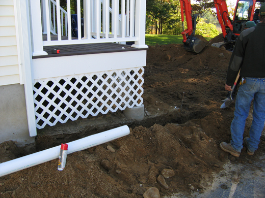 Trench dug around a house with a pipe sitting to the side waiting to be installed in the trench.