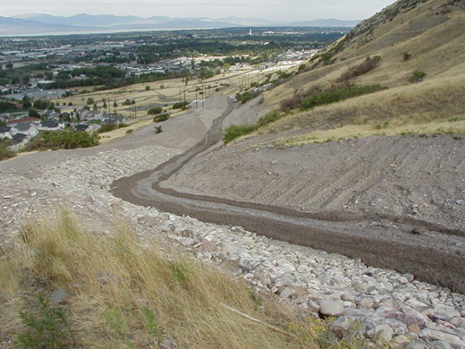 Photo taken from midway up a mountain looking down into a valley, showing the path of an alluvial fan flood.