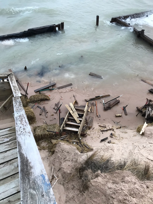 Lake water intruding beyond a wooden seawall with wood debris also strewn about a small sand beach area.