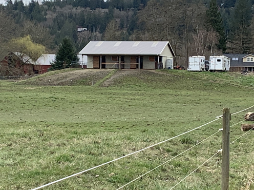 A agricultural buildings elevated on fill in a field with room for trailers; other structures visible in the background.