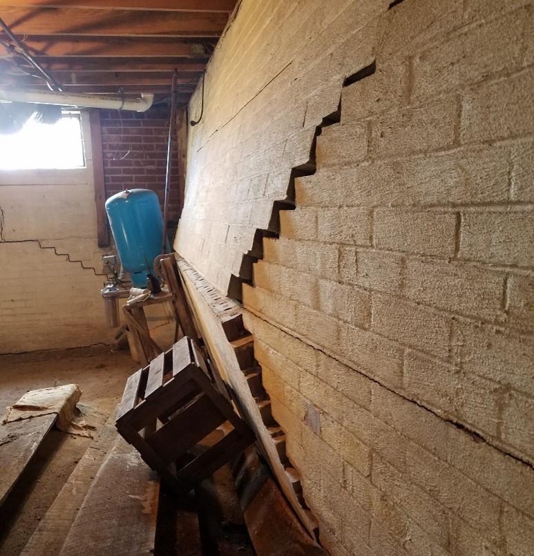Concrete masonry unit basements walls that have major cracks due to bowing walls, the cracks start from the center of the wall and stair step to the ground and ceiling diagonally in an X