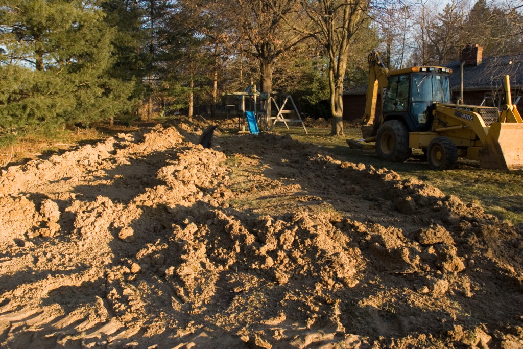 Disturbed soil which will become a leach field in a backyard with a swing set visible in the background and a construction vehicle at rest on the right.