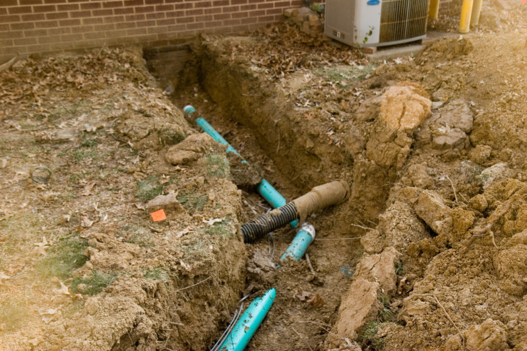 A green pipe which runs from the house to the septic tank. Also pictured, a curtain drain along the back of the house that had to be cut through and repaired for the green pipe to run properly.