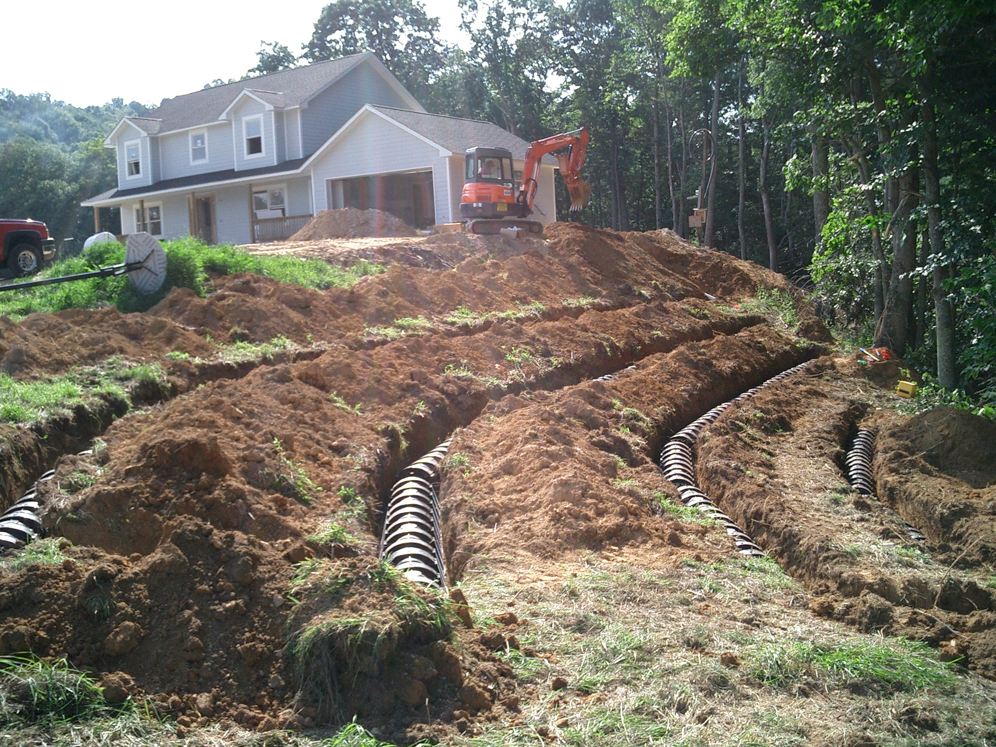 Four lines are run on a steep slope to the right of a house on the top of the hill. Septic system installation can be a challenge when steep slopes need to be considered.