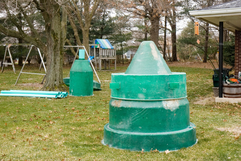 Two small green septic tanks sitting in a backyard waiting to the installed. The backyard has a treehouse and swing set