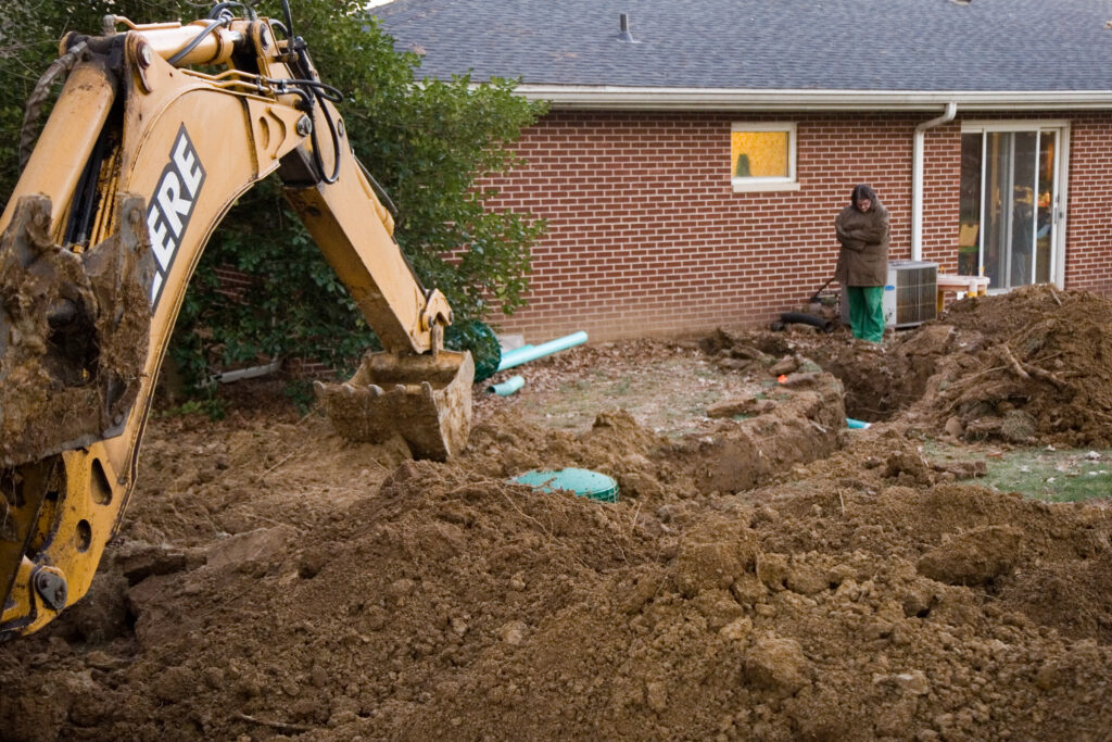 A construction vehicle covers the installed main septic tank in soil while the property owner looks on.