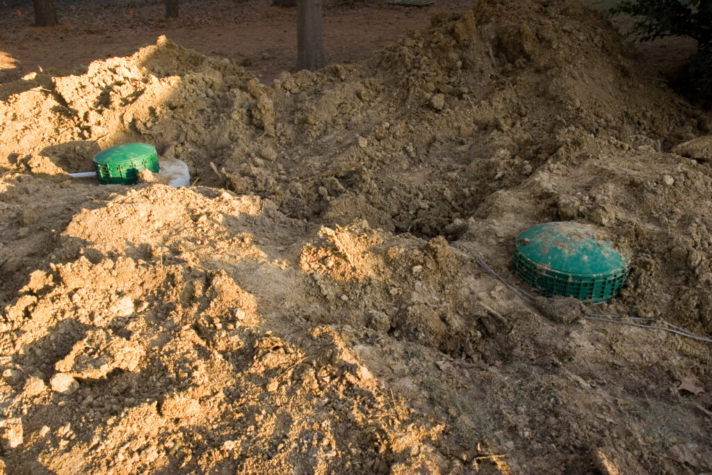 The tops of the primary and secondary septic tanks are visible after being buried in soil.