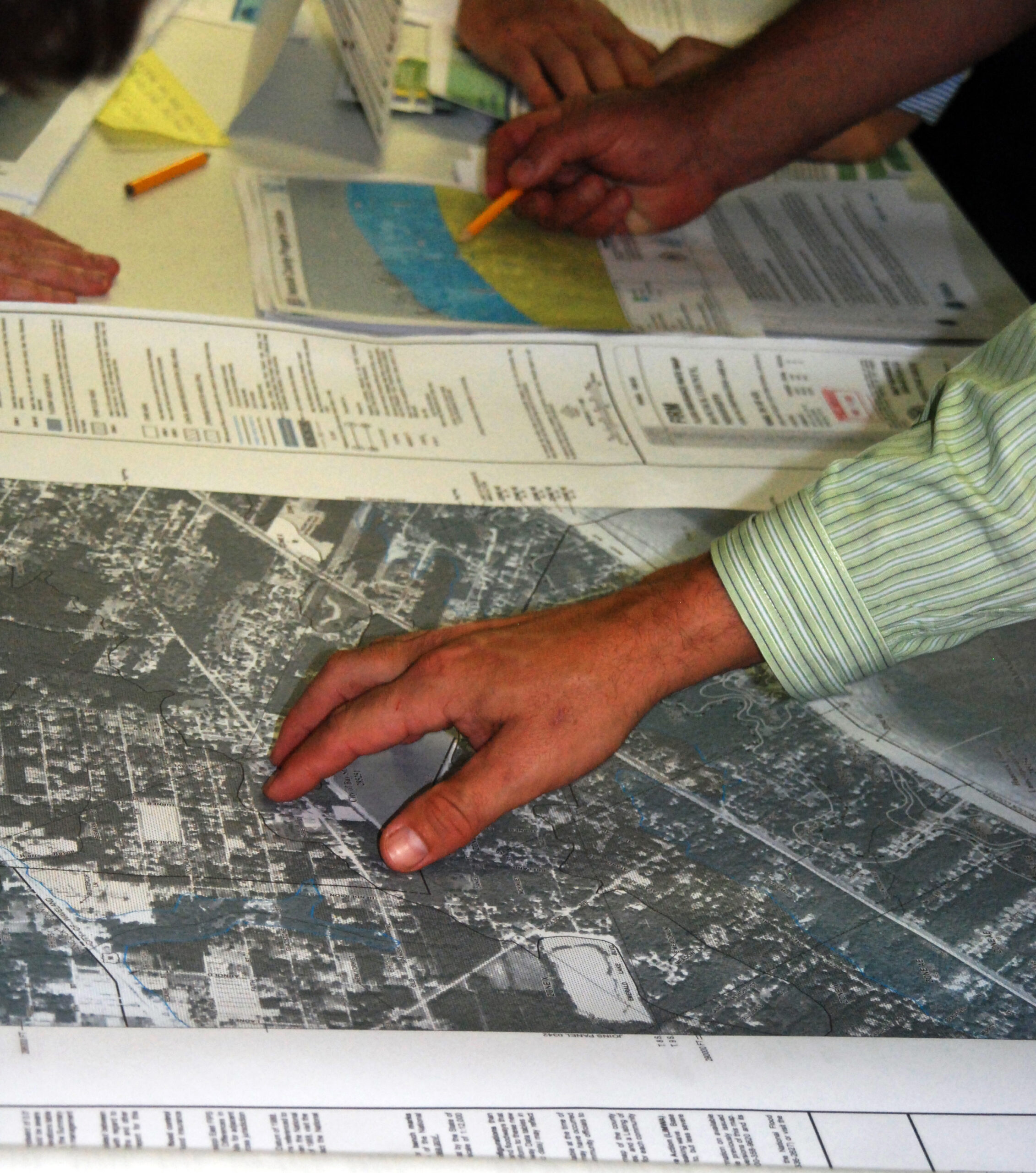 The event kicked off community adoption of the Digital Flood Insurance Rate Maps to meet requirements of the National Flood Insurance Program. Pictured are people's hands as they peruse over printed flood maps.